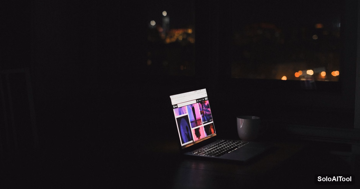 A laptop glowing alone on a desk in a dark room with city lights through the window at night